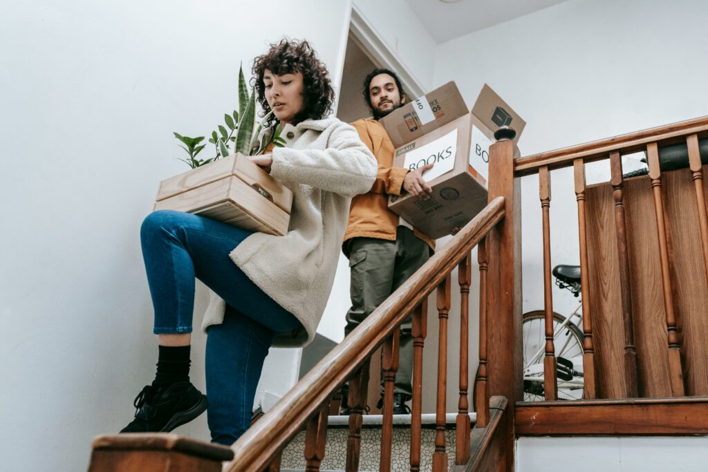 A couple carrying boxes up the stairs, indicating a move into a new home.