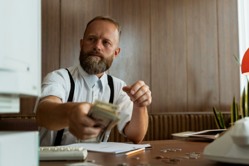 Man at a desk counting a stack of cash, with a look of concern.