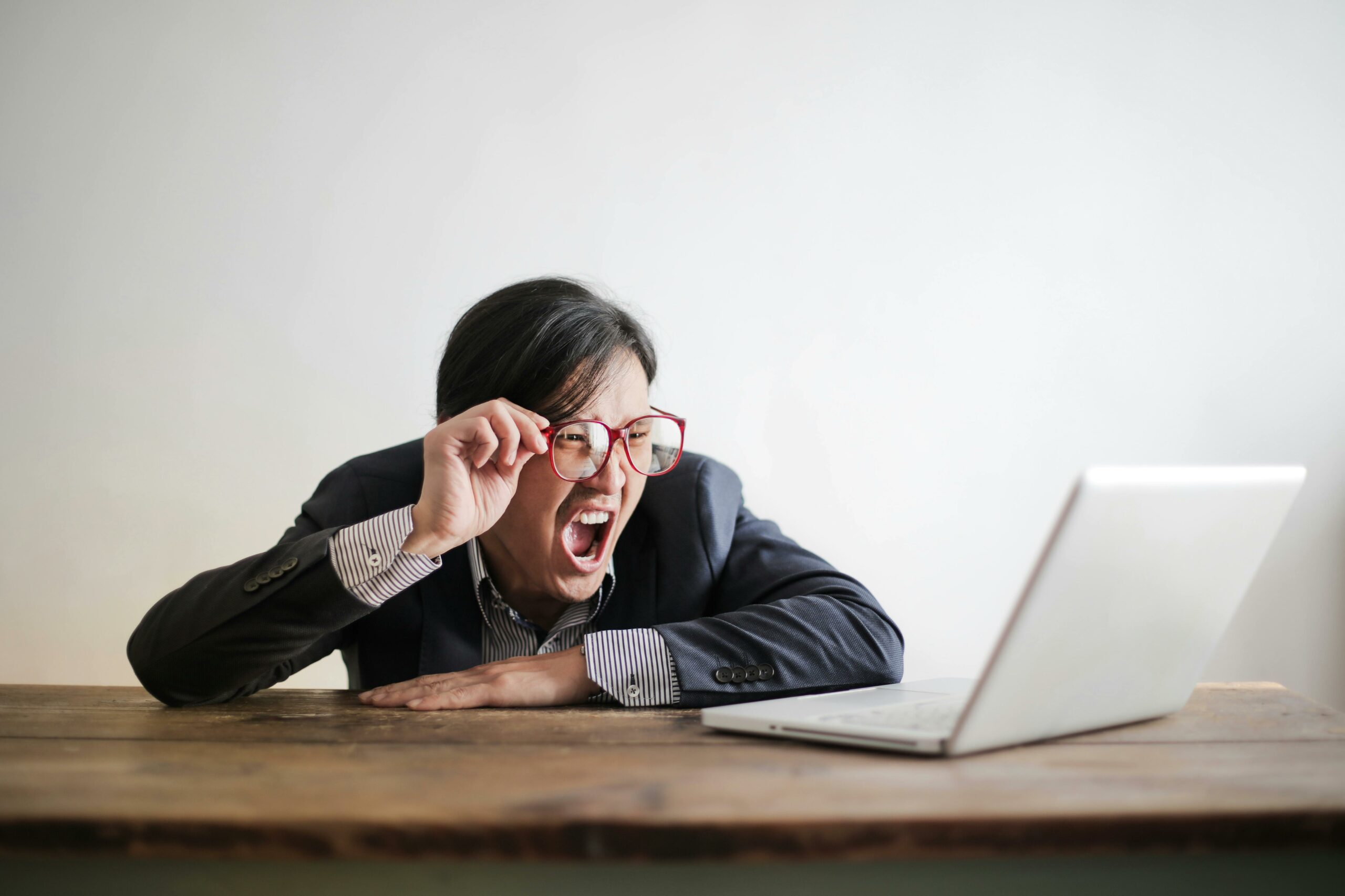 Business person with glasses shouting in frustration at a laptop screen.