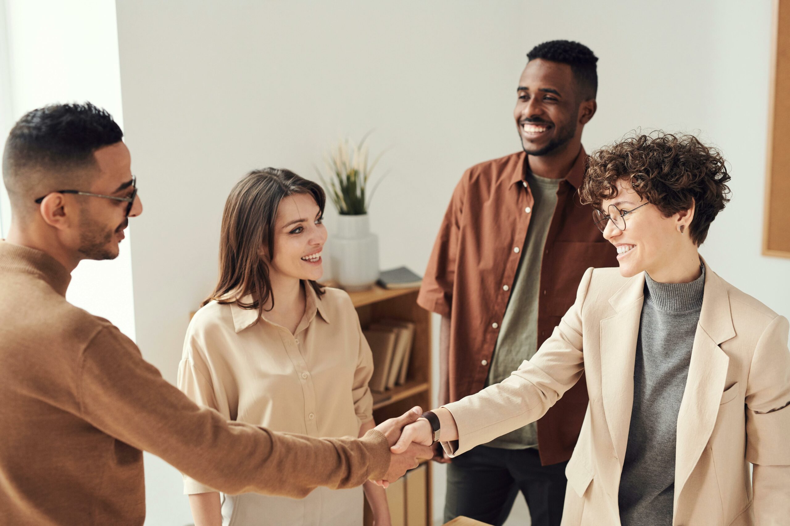 Four smiling people engaging in a friendly handshake in a bright office setting.