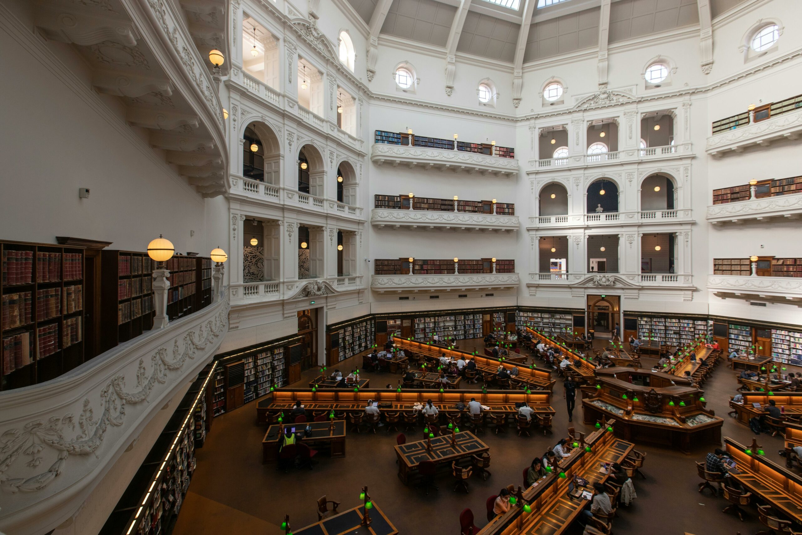 Interior of a grand library with rows of reading tables and multiple levels of bookshelves.