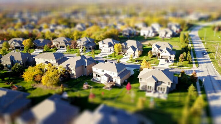 Tilt-shift photography of a residential neighborhood with sunlit homes and autumnal trees.