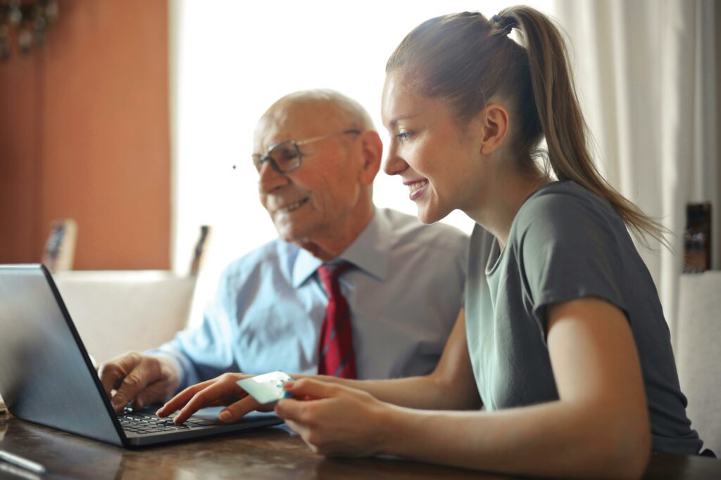 Smiling young woman and elderly man with glasses looking at a laptop screen, engaged in financial planning