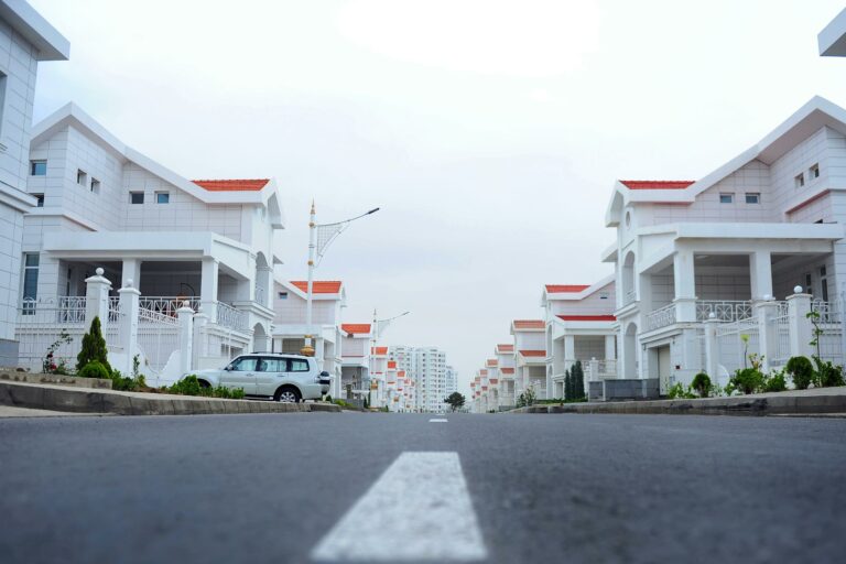 Street-level view of a row of uniform white houses with red roofs in a suburban neighborhood.