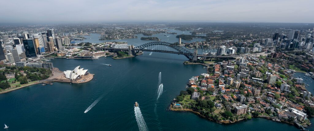 Aerial view of Sydney Harbour featuring the Sydney Opera House and Sydney Harbour Bridge, illustrating the skyline and waterfront homes, representing the dynamic real estate market and Sydney house prices.